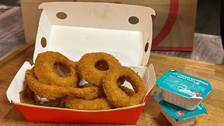 Jack in the Box onion rings in carton with two containers of buttermilk ranch sauce.
