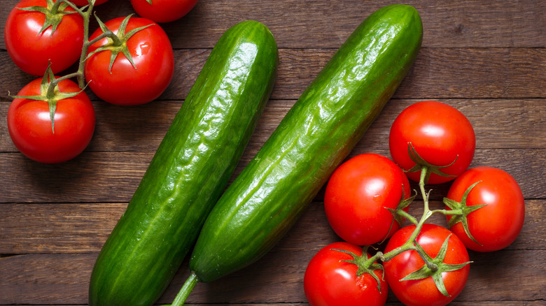 Raw cucumbers and tomatoes on a wooden cutting board.