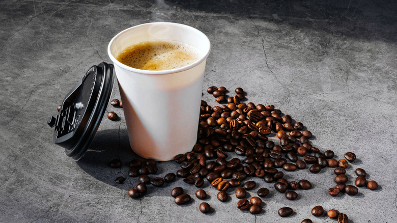 Steaming to-go cup of coffee cup surrounded by whole beans