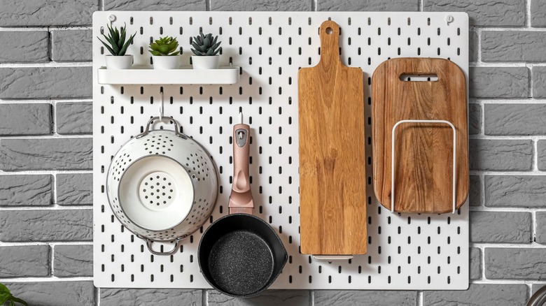Pegboard hanging cookware and cutting boards on gray brick wall
