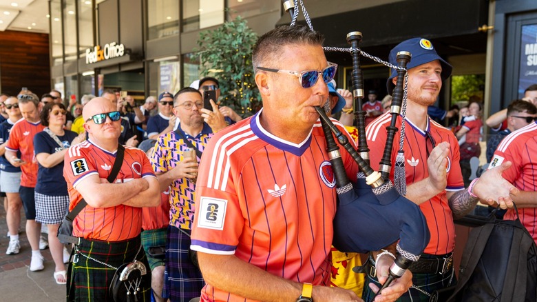 Scottish soccer fan playing bagpipes while waiting with other to enter a pub
