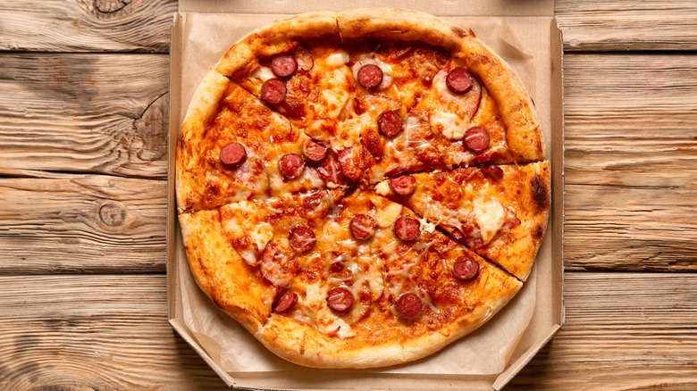 Pizza with meat topping in carboard box on wood surface