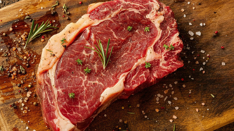 A raw slab of seasoned ribeye on a wooden board.