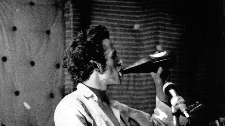 Joe Strummer from The Clash drinking a beer while holding a guitar