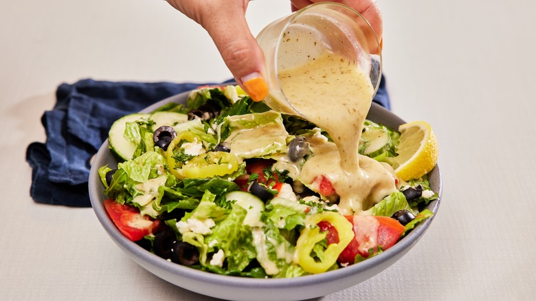 person pouring individual cup of dressing on top of salad