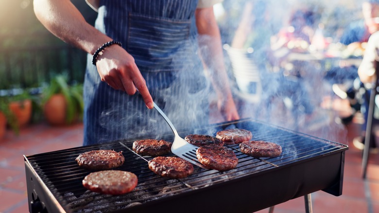 man flipping burger patties on outdoor grill