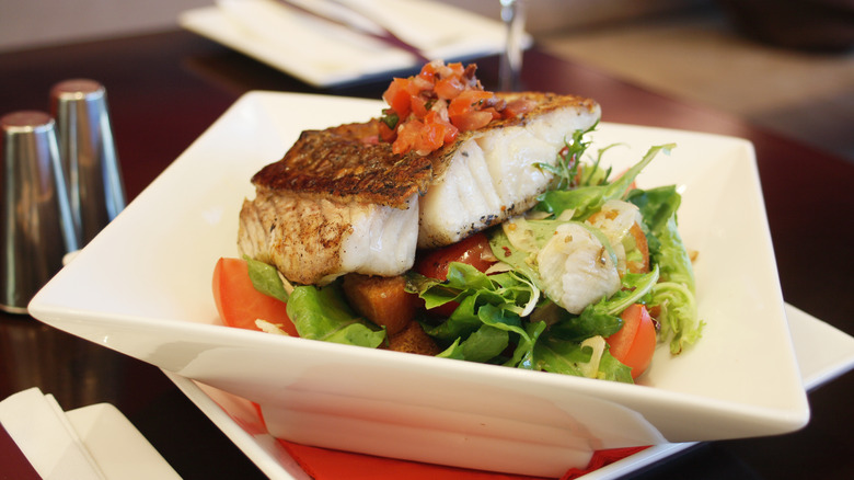 Piece of pan-fried barramundi fish on a lettuce and tomato salad
