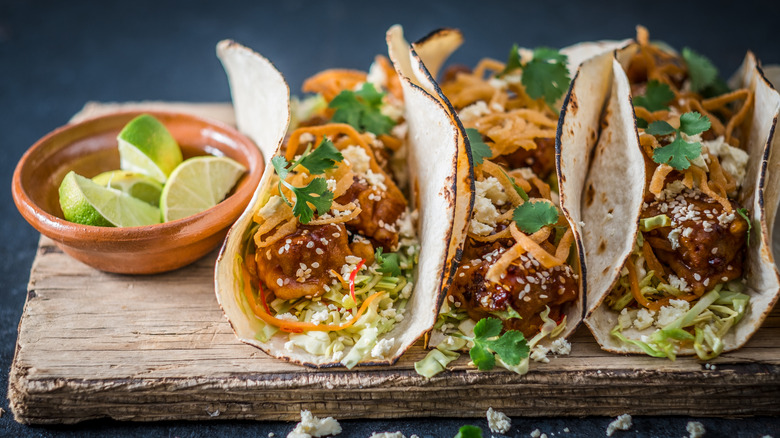 Chicken tacos on a wooden cutting board with a bowl of quartered limes.
