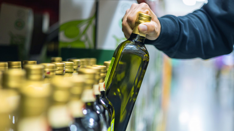 A man pulls a glass bottle of olive oil from the shelf at the grocery store.