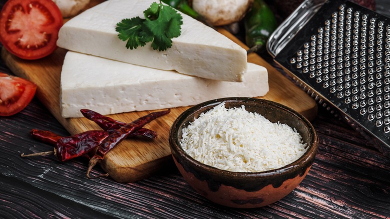 Wedges of Cotija cheese next to bowl of shredded cheese and grater