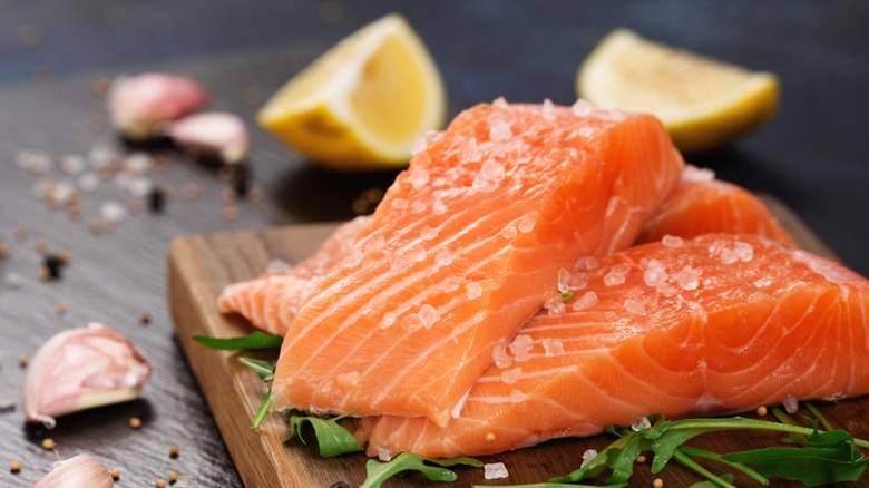 Raw filets of salmon on a wooden board with lemon wedges and garlic cloves in the background