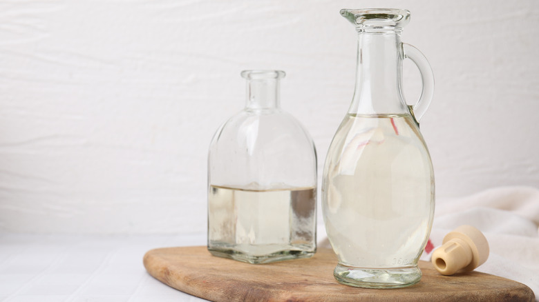Glass jugs of vinegar on a wooden board against a white backdrop