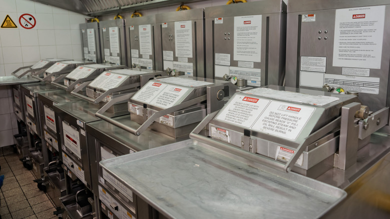 Row of industrial fryers with closed steel lids and warning labels