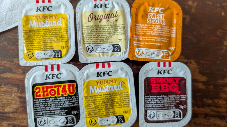 Six plastic containers of different KFC dipping sauces on a wooden table