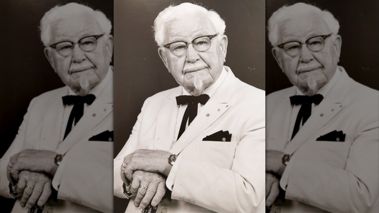 Black and white portrait of Colonel Sanders with a white goatee, black string tie, and a white suit