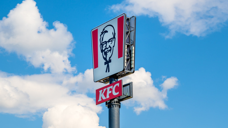 A red and white KFC sign against a bright blue sky with puffy white clouds
