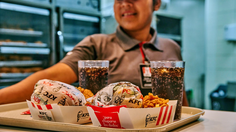 A KFC employee sliding a tray with two paper boats filled with chicken and two sodas