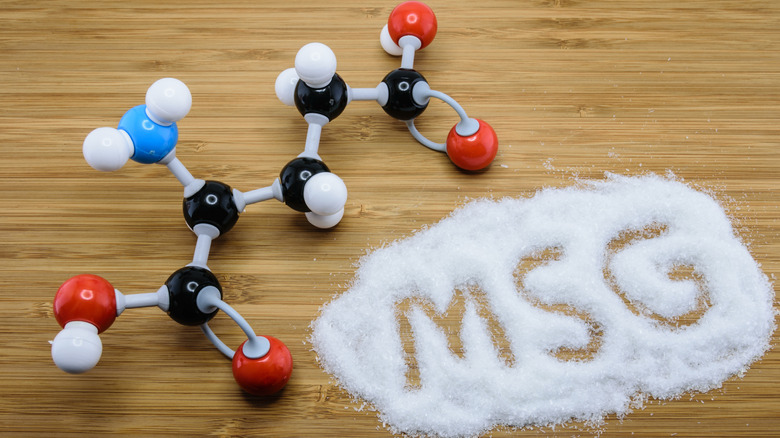 A model of a molecule on a wood table next to white powder with the letters M-S-G written in it