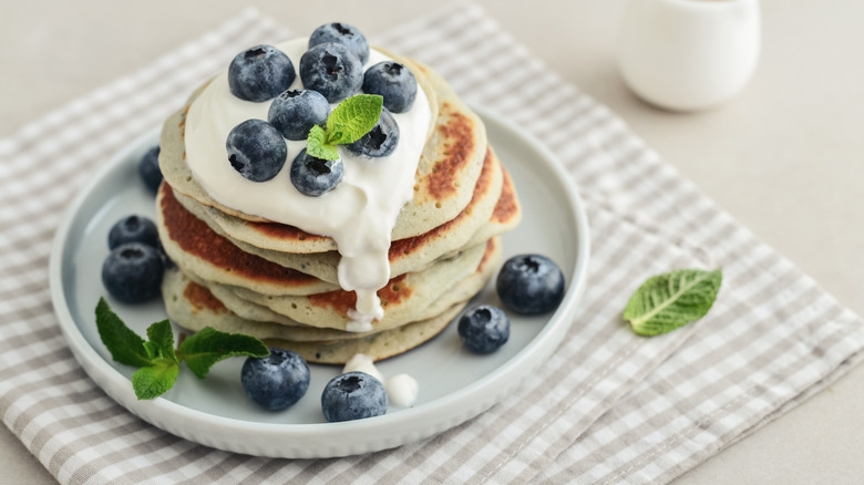 stack of pancakes with whipped cream, blueberries, and a sprig of mint on a small plate