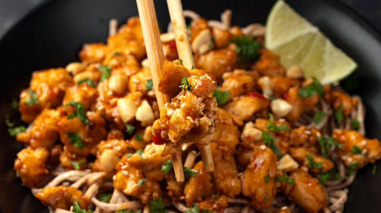 Tofu-noodle stir-fry in a bowl with chopsticks and a lime wedge
