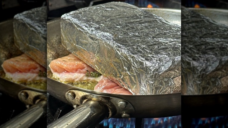 Foil-wrapped brick on top of chicken searing in a pan
