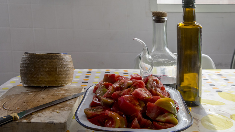 Platter of sliced tomatoes on table with board, olive oil