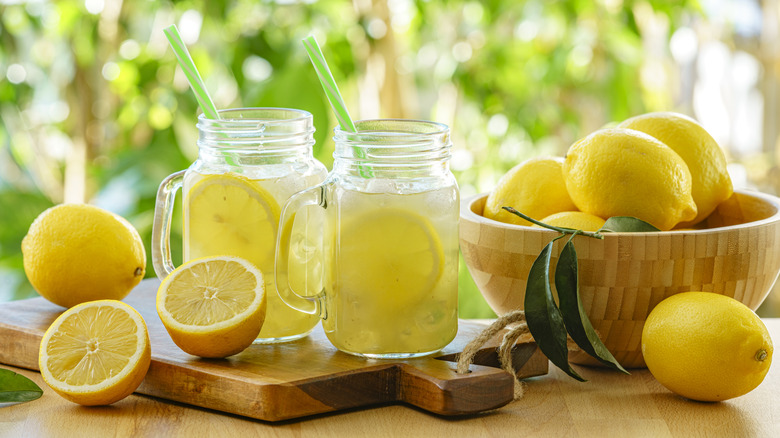 Two mason jars of lemonade with straws next to whole and halved lemons