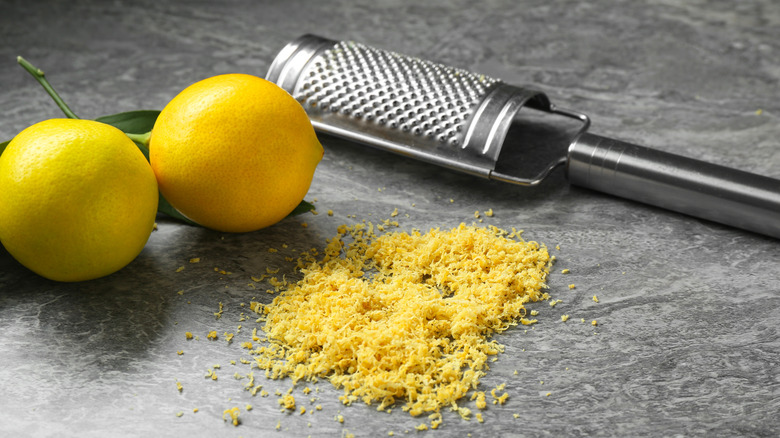 Two lemons, pile of lemon zest and metal grater on gray