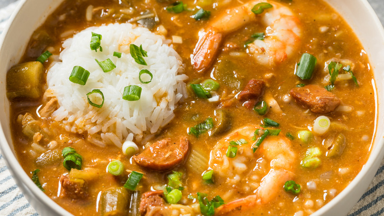 Closeup of bowl of shrimp and sausage gumbo with rice and chopped scallions on top