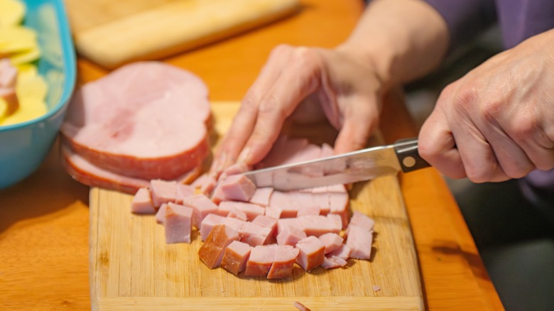 Close-up of ham being cut into cubes with a serrated knife
