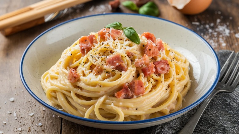 White and blue bowl of spaghetti with cheese, pepper, bacon