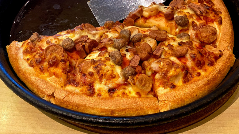Pizza Hut pan pizza in baking dish with metal spatula.