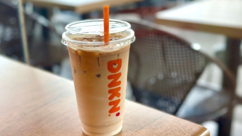 A large iced latte from Dunkin' on a wooden table.