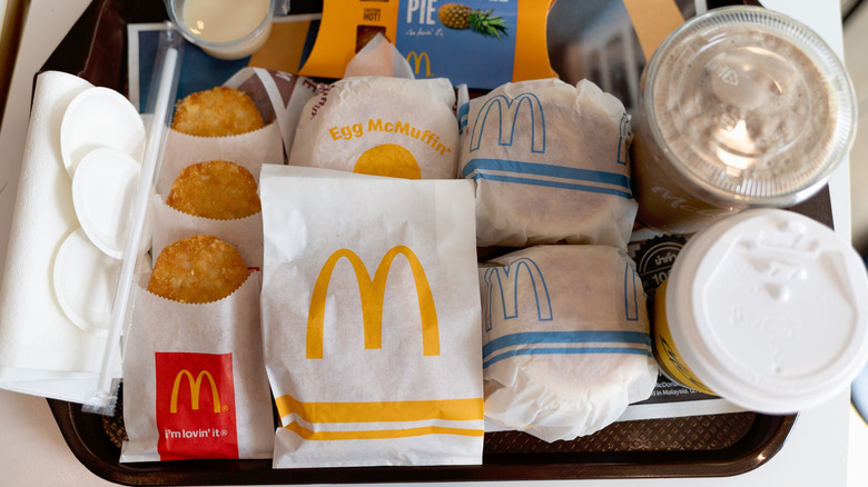 Assorted McDonald's breakfast foods on tray, including hash browns, wrapped Egg McMuffins, and drinks