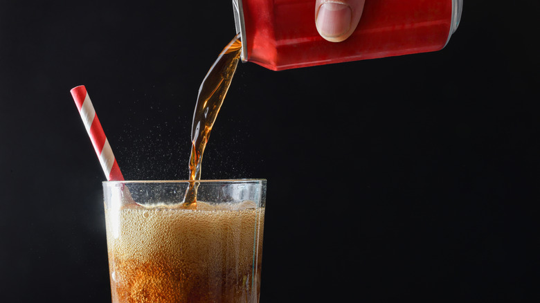 A hand pouring cola from red can into a glass with ice