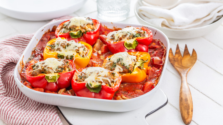 Stuffed bell peppers in casserole dish on tomato sauce.