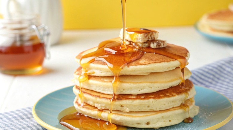 A stack of pancakes being drizzled with syrup.
