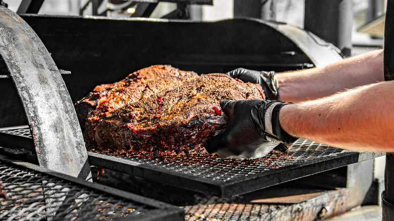 Gloved hands putting seasoned brisket in smoker