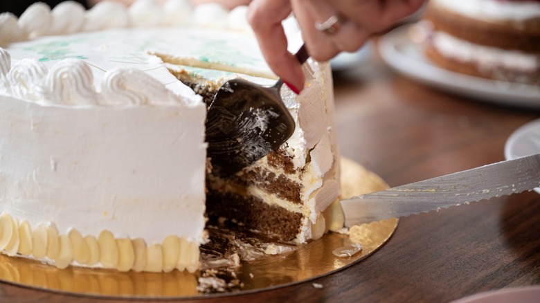 Person slicing white cake with serrated knife