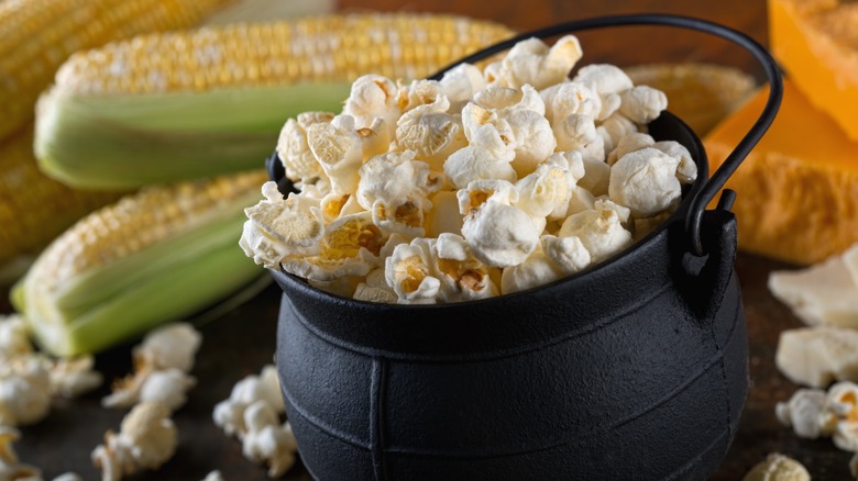 White cheddar popcorn in a small black cauldron near ears of corn