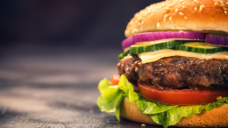 A close-up of a burger with cheese, lettuce, tomatoes, pickles and onions on it