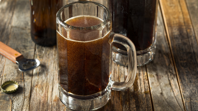 A glass of homemade root beer with measuring spoons on a wooden table