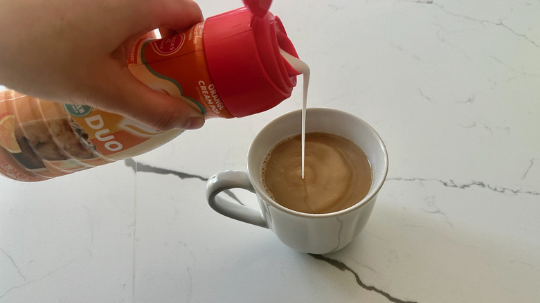 coffee creamer being poured into coffee cup