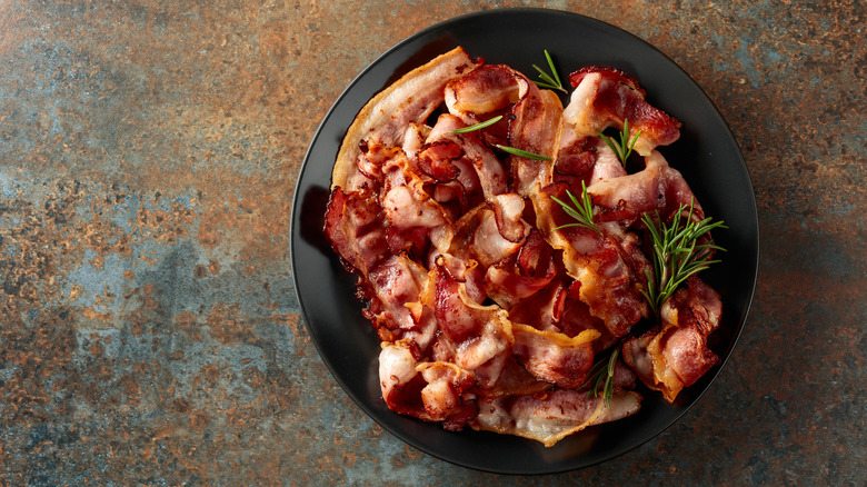 Top view of fried bacon with rosemary on a black plate.