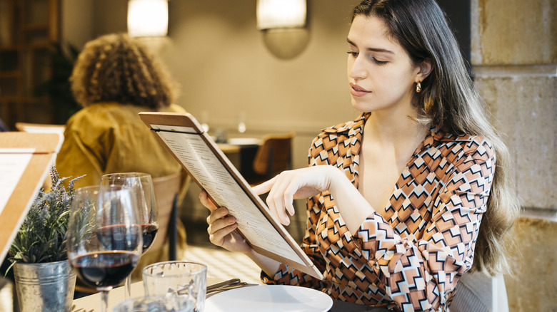A woman sitting at a restaurant reading a menu