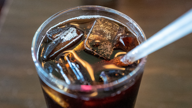 A close-up shot of a bubbly glass of cola with ice and a straw