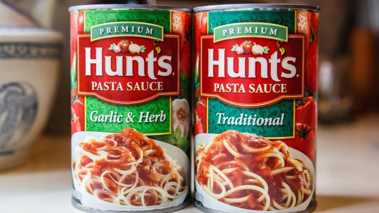 Two cans of Hunt's pasta sauce sitting in front of some kitchen items.