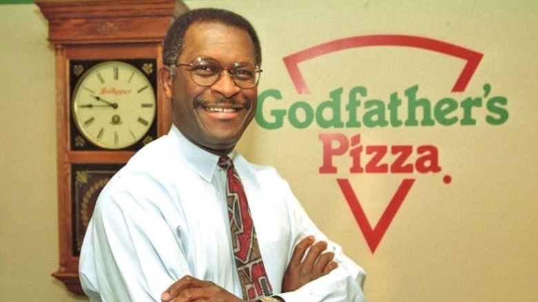 Herman Cain, then president of Godfather's Pizza, poses near the store's logo.