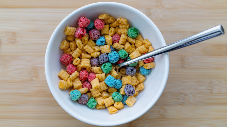 A bowl of colorful puffed cereal with a spoon on a wooden surface