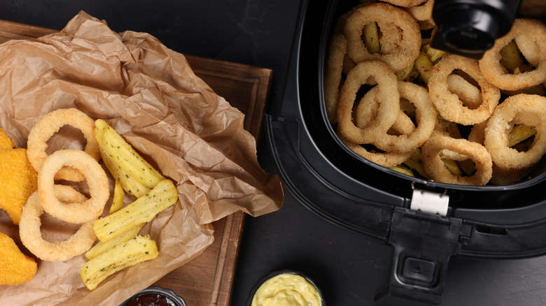 Fried calamari rings in an air fryer next to finished calamari in brown paper